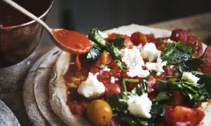 Sos pomidorowy dodawany łyżką do pizzy z serem i bazylią.