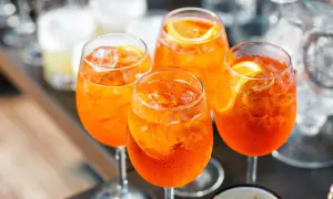 Cztery orzeźwiające drinki z aperolem i lodem, ozdobione plasterkami pomarańczy.