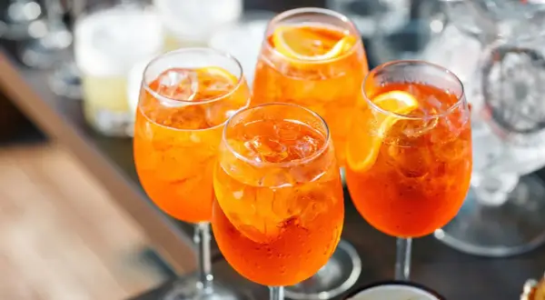 Cztery orzeźwiające drinki z aperolem i lodem, ozdobione plasterkami pomarańczy.