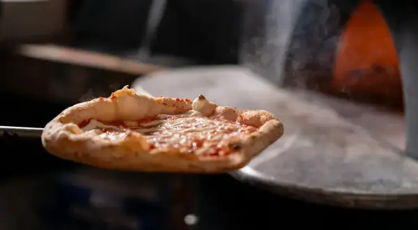 Gorąca pizza z serem i sosem pomidorowym wyjmowana z pieca.